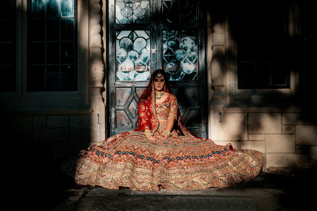 A stunning bride in a traditional bridal gown poses elegantly by an ornate doorway, showcasing intricate jewelry.